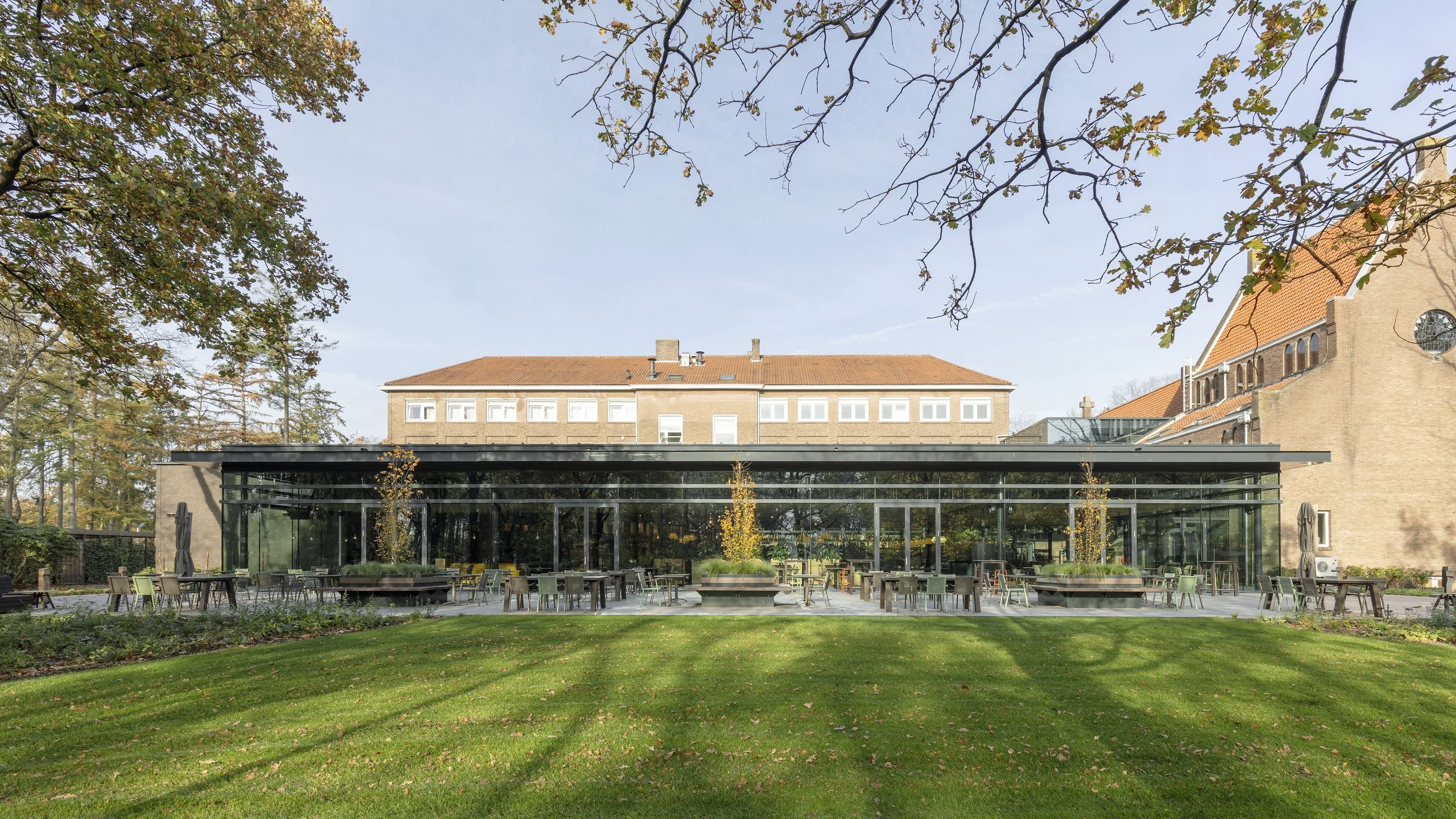 Het glazen paviljoen van ProefLokaal de Wereld met terras aan de tuinzijde van conferentiehotel Kontakt der Kontinenten in Soesterberg, gezien vanaf het gazon.